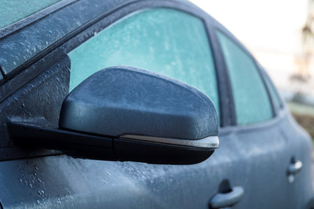 A portrait of a frozen side mirror of a completely frozen car during winter time. The ice first needs to melt or be removed before the driver can safely start the journey.の写真素材