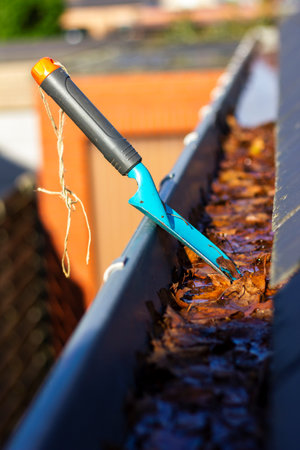 A portrait of a roof gutter full of fallen autumn leaves on a sunny day with a small blue garden shovel in it of someone who is cleaning the gutter during the fall season annual chore.の写真素材