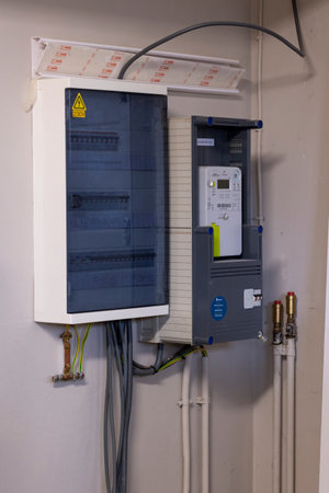 Brecht, Belgium - January 26, 2023: Portrait of a new installed Belgian digital electricity kilowatt hour meter next to a fuse box with some electrical wiring running out of it.のeditorial素材