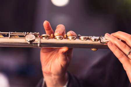 A portrait of the fingers of a hand of a flutist musician gripping down on the valves of a metal silver flute to play a note of a musical piece during a concert.の写真素材