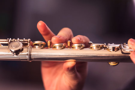 A portrait of the fingers of a hand of a flutist musician pressing down on the valves of a metal silver flute to play a note of a musical piece during a concert.の写真素材