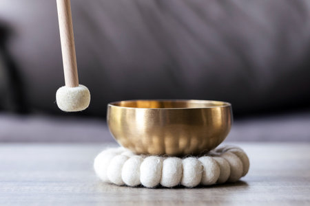 A close portrait of a mallet about to hit a Tibetan singing bowl or himalayan bowl to produce a relaxing sound for meditation, relaxation and to relieve stress. It is an alternative medicine.の写真素材