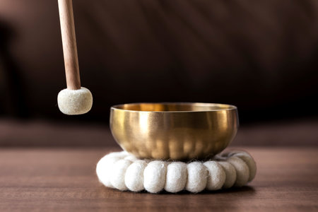 A close up of a mallet about to hit a Tibetan singing bowl or himalayan bowl to produce a relaxing sound for meditation, relaxation and to relieve stress. It is an alternative medicine.の写真素材