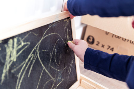 A portrait of a toddler scribbling, drawing or doodling a bit on a chalkboard. The child is writing on the blackboard and has a yellow piece of chalk in its hand.の写真素材