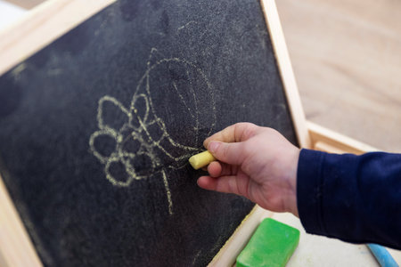 A close up portrait of a toddler scribbling, drawing or doodling a bit on a chalkboard. The child is writing on the blackboard and has a yellow piece of chalk in its hand.の写真素材