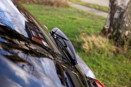 A close up portrait of the windshield wiper attached to the rear window of a dark blue car. The device is used to clear rain or snow from the window so the driver gets a clear view again.の写真素材
