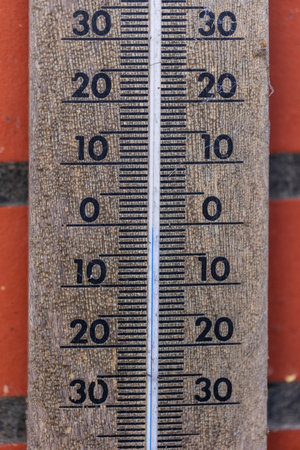 A close up portrait of a thermometer gauge showing a temperature measurement of zero degrees celcius. The instrument is hanging on a brick wall.の写真素材