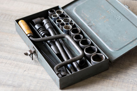 A portrait of an open old metal toolbox with a socket wrench with a wooden handle in it. It contains a lot of different sizes of sockets to use with the tool, perfect for use by a mechanic.の写真素材
