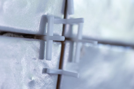 A close up portrait of white plastic joint spacers placed in the junctures inbetween ceramic tiles which have been installed on a wall with tile adhesive.の写真素材
