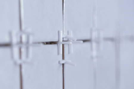 A close up portrait of plastic white joint spacers placed in the juncture of a recently tiled wall to preserve the distance so the ceramic tiles are installed in a nice pattern.の写真素材