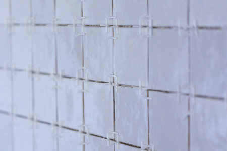 A portrait of a tile wall under construction. The wall is being tiled with small ceramic rectangular tiles. There are still plastic white joint spacers in between the junctures of the tiles.の写真素材