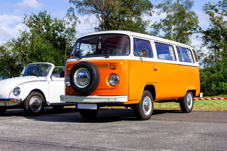 Oostmalle, Belgium - August 19 2023: An orange and white vintage old timer volkswagen split bus, camper, minibus or minivan standing parked on the street. The VW car has a spare tire at the front.のeditorial素材