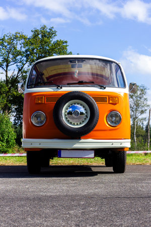 Oostmalle, Belgium - August 19 2023: An orange and white vintage old timer volkswagen split bus, minivan, minibus or camper standing parked on the street. The VW car has a spare tire at the front.のeditorial素材