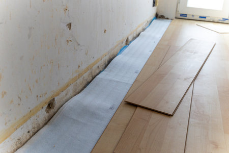 A portrait of stacked wood imitation laminate floorboards lying on some sound isolation ready to be installed to create a wooden floor in a room of a house on a screed floor.の写真素材