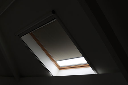A portrait of a Velux skylight window almost closed by a blinding. The blind is making the room dark, but still lets some light enter. This also keeps warmth outside and keeps it cool inside.の写真素材