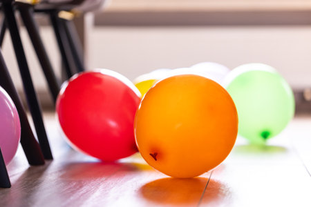 Multiple colorful balloons lying on a living room floor indoor of a house in between the chairs of the table. The fun decorations are ready for a home birthday party or anniversary celebration.の写真素材