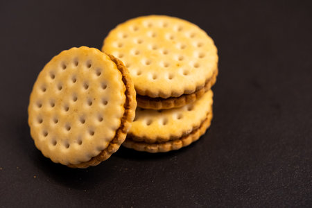 A top down closeup of delicious round cookies stacked on top of each other with one fallen off on a kitchen counter. The tasty snack has a biscuit on each side and is filled with chocolate cream.の写真素材