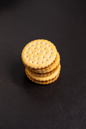 A top down vertical portrait of delicious round cookies with holes stacked on top of each other on a kitchen counter. The tasty snack has a biscuit on each side and is filled with chocolate cream.の写真素材