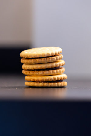 A portrait of delicious round cookies with holes stacked on top of each other on a kitchen counter. The tasty snack has a biscuit on each side and is filled with chocolate cream.の写真素材