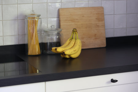 A portrait of a bunch of yellow bananas with som brown spots lying on a black kitchen countertop....
