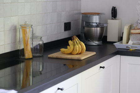A portrait of a bunch of yellow bananas lying on a wooden cutting board on a black kitchen countertop. The delicious energizing food is ready to eat and ideal before sport.の写真素材