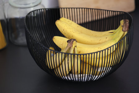 A closeup portrait of a bunch of bananas lying in a decorative black metal bowl on a black kitchen counter. The healthy energizing food is ready to be eaten before a sport activity.の写真素材