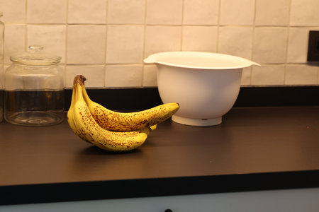A portrait of a bunch of yellow bananas with som brown spots lying on a black kitchen countertop. The delicious energizing food is ready to eat and ideal before a sport activity.の写真素材