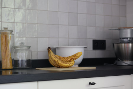 A portrait of a bunch of yellow bananas lying on a white plastic cutting board on a black kitchen countertop. The delicious energizing food is ready to eat and ideal before sport.の写真素材