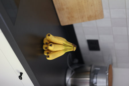 A portrait of a bunch of yellow bananas with som brown spots lying on a black kitchen countertop. The delicious energizing food is ready to eat and ideal before a sport activity.の写真素材
