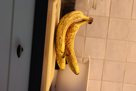 A vertical of a bunch of yellow bananas with brown spots lying on a white plastic cutting board on a black kitchen countertop. The delicious energizing food is ready to eat and ideal before sport.の写真素材