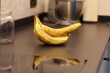 A portrait of a bunch of yellow bananas with som brown spots lying on a black kitchen countertop. The delicious energizing food is ready to eat and ideal before a sport activity.の写真素材