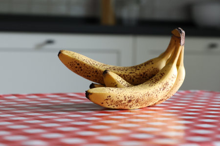 A closeup portrait of yellow bananas with some brown spots lying on a red and white table cloth on a kitchen table. The delicious energizing food is ready to be eaten.の写真素材