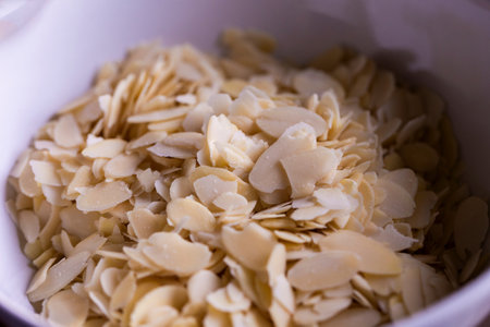 A delicious food portrait of a white bowl full of almond flakes used by a baker to create tasty cookies or pastries. The chopped up crunchy cooking and baking ingredient is ready to be used.の写真素材