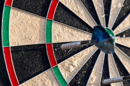 A portrait of a part of a dartboard game outside on a sunny day, with darts sticking in it. the bull is also visible. the darts are ready to be thrown in a game or match.の写真素材
