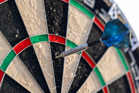 A closeup portrait of a part of a dartboard game standing outdoors on a sunny day, with one dart sticking in it. the bull is also visible. the darts are ready to be thrown in a game or match.の写真素材