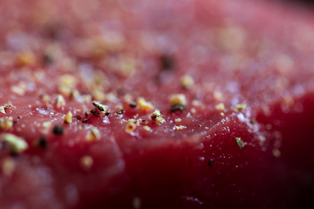 A macro portrait of the seasoning on a red raw steak being prepared or cooked in a frying pan. The delicious meat has pepper and salt on it for a perfect meal or dinner.の写真素材