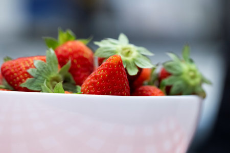 A closeup portrait of a bunch of red tasty fresh strawberies with the green top in a white bowl. The delicious fruit is ready to be eaten.の写真素材
