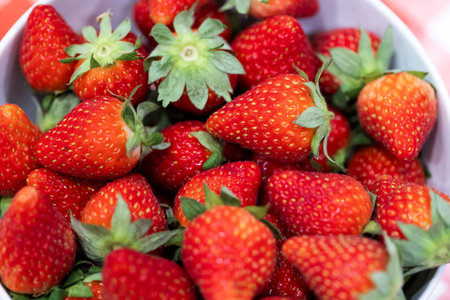 A closeup of a bunch of red delicious fresh strawberies with the green top in a white bowl. The tasty fruit is ready to be eaten.の写真素材