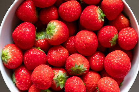 A close-up of fresh, ripe strawberries with vivid red color and green leaves in a white bowl, showcasing their juicy texture and natural beauty. The delicious fruit is ready to eat.の写真素材