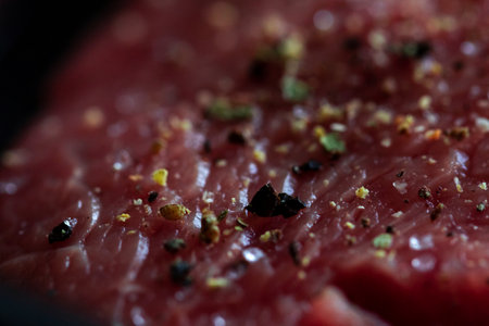 A close up portrait of the seasoning on a red raw steak being prepared or cooked in a frying pan. The delicious meat has salt and pepper on it for a perfect meal or dinner.の写真素材