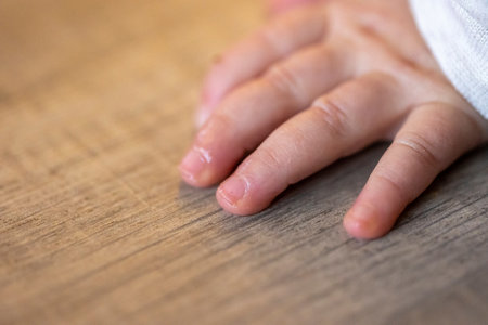 A closeup portrait of the small fingers of a cute baby lying on a wooden floor while it is crawling. The tiny hand of the newborn is flat on the surface.の写真素材