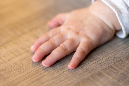 A portrait of the small hand of a cute baby lying on a wooden floor while it is crawling. The tiny fingers of the newborn are all flat on the surface.の写真素材