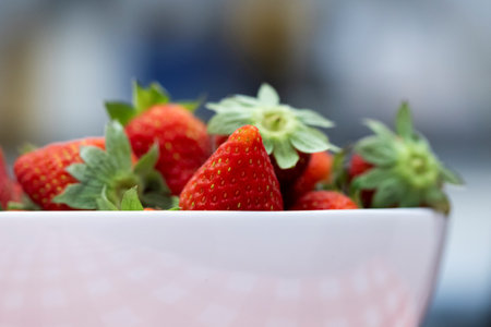 A portrait of a bunch of tasty red fresh strawberies with the green top in a white bowl. The delicious fruit is ready to be eaten.の写真素材