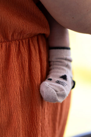 A portrait of the cute leg and foot of a baby wearing a cozy sock pressed safely against the caring mother who is carying the small child.の写真素材