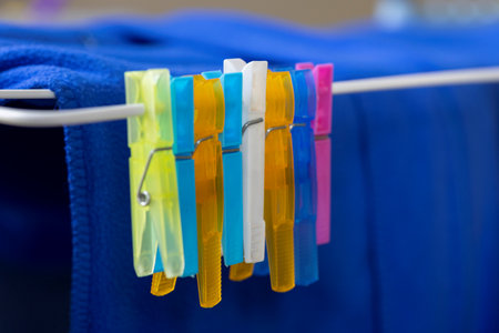 A portrait of a lot of colorful washing pegs or pins hanging on a rail of a drying rack. These clamps are ideal to hang clothing up to dry.の写真素材