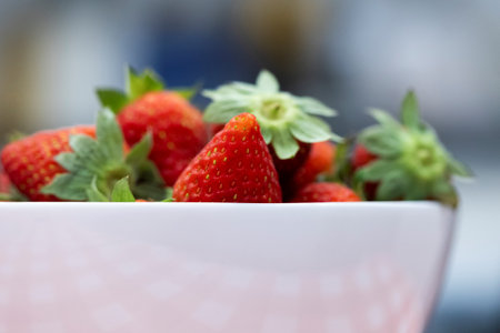 A closeup portrait of a bunch of tasty red fresh strawberies with the green top in a white bowl. The delicious fruit is ready to be eaten.の写真素材