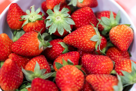 A portrait of a bunch of red delicious fresh strawberies with the green top in a white bowl. The tasty fruit is ready to be eaten.の写真素材