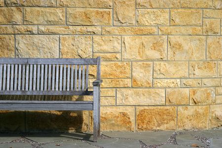 Park bench against stone wall with strong sun and shadows.の写真素材