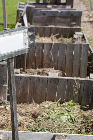 Several compost bins in a row at a community garden with blank sign post.