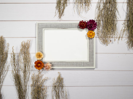 Top view of empty photo frame with dry colorful flowers over a white wooden tableの写真素材